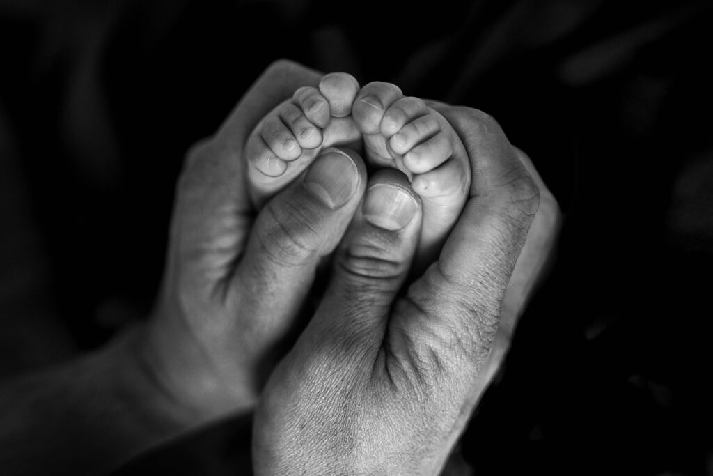 black and white image of dad holding baby toes in hands