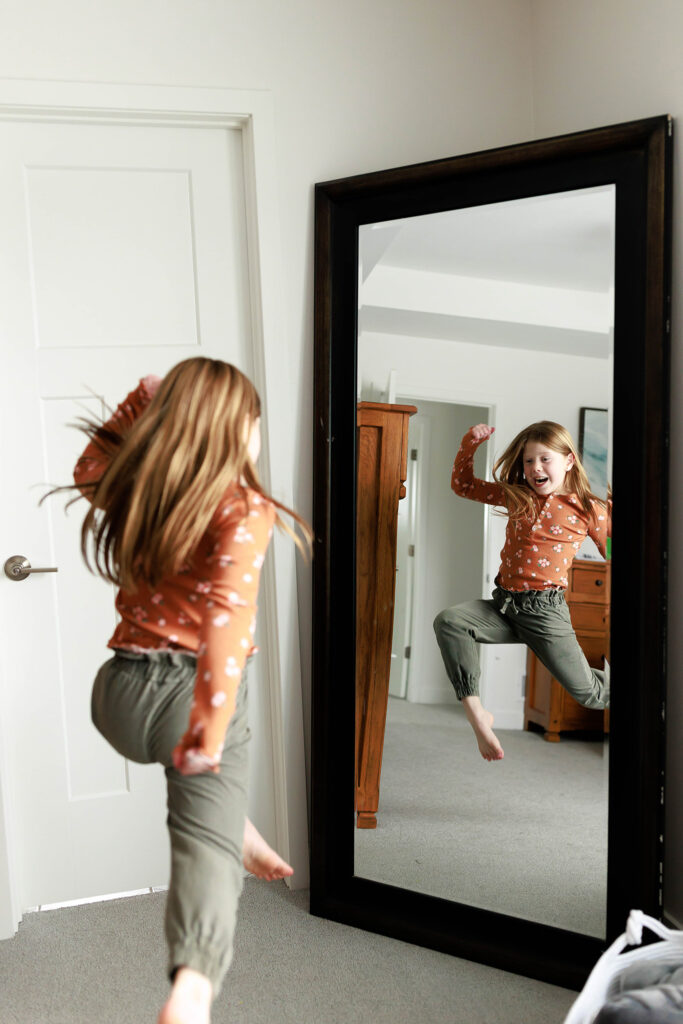 young girl jumping in front of mirror watching her reflection