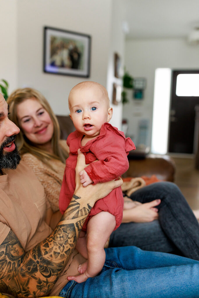baby girl in romper with mom and dad in home photo shoot
