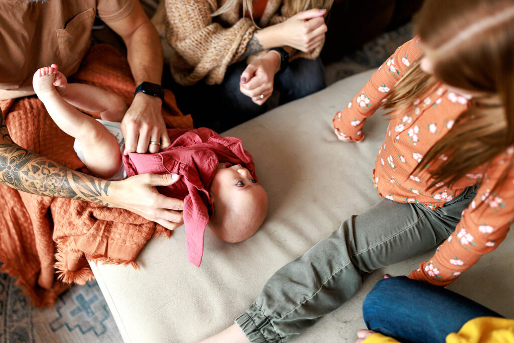 dressing baby in pink romper on ottoman in home photo shoot