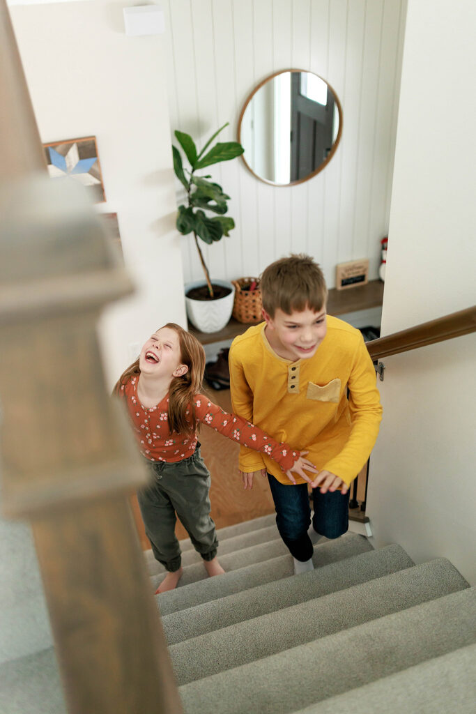 brother and sister giggling as they race up the stairs of their home