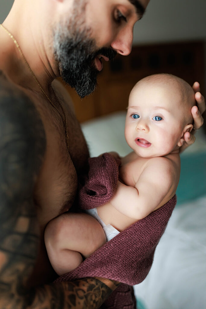 shirtless dad holding baby with blue eyes