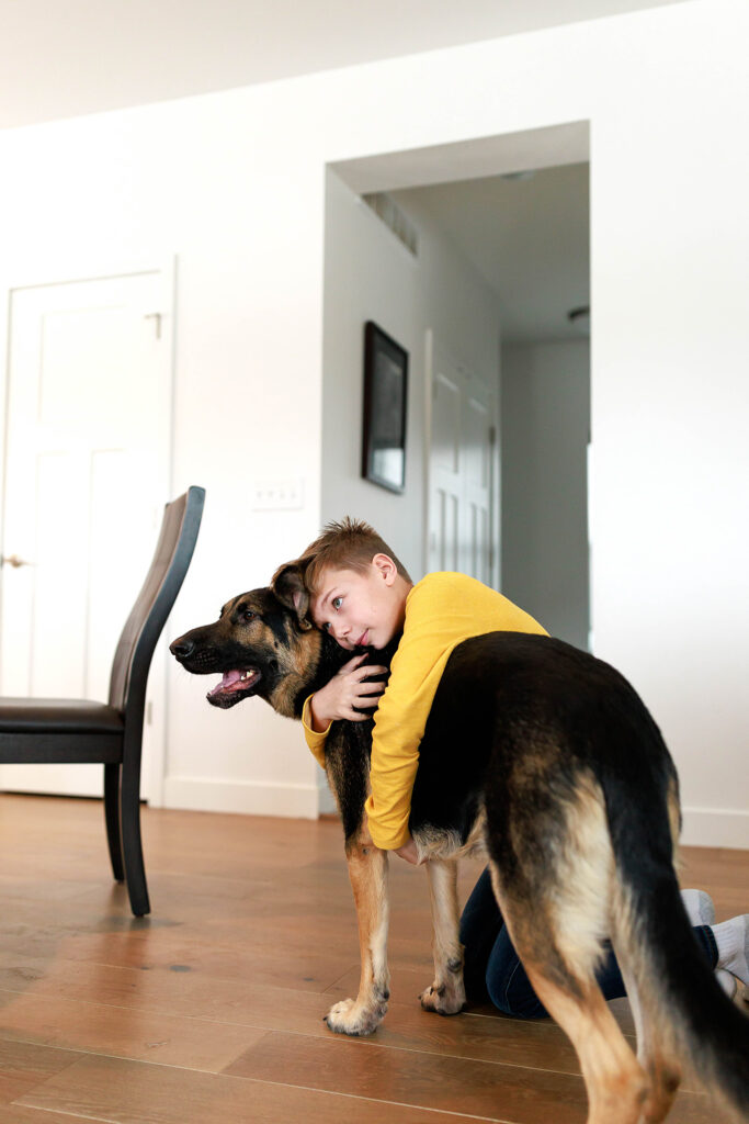 young boy in yellow shirt hugging family dog in dining room