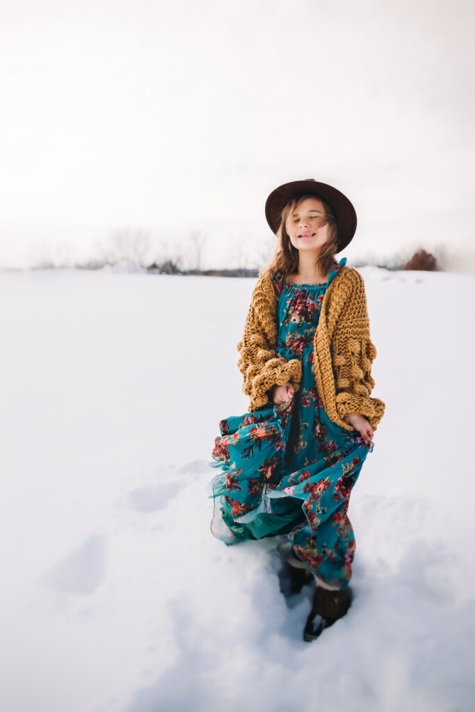 little girl in blue floral dress posing in snowy backdrop for winter photos