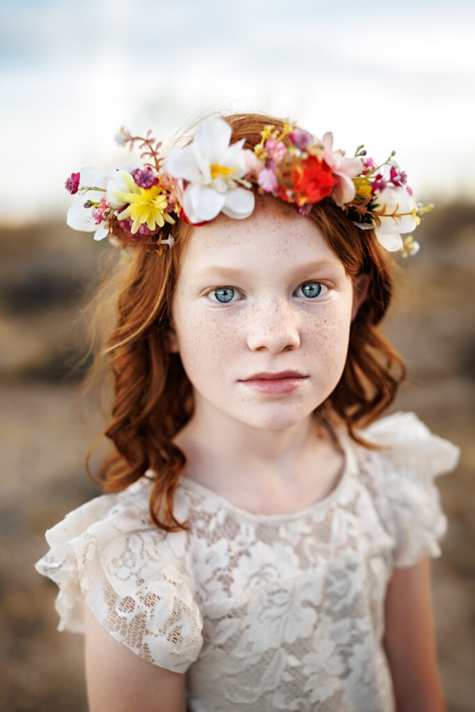 portrait of red headed girl with blue eyes and flower crown wearing white lace dress in phoenix desert