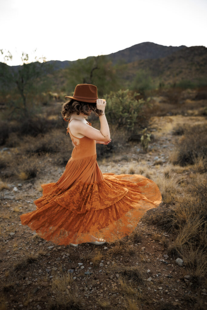 girl twirling in rust colored boho dress with hand on fedora