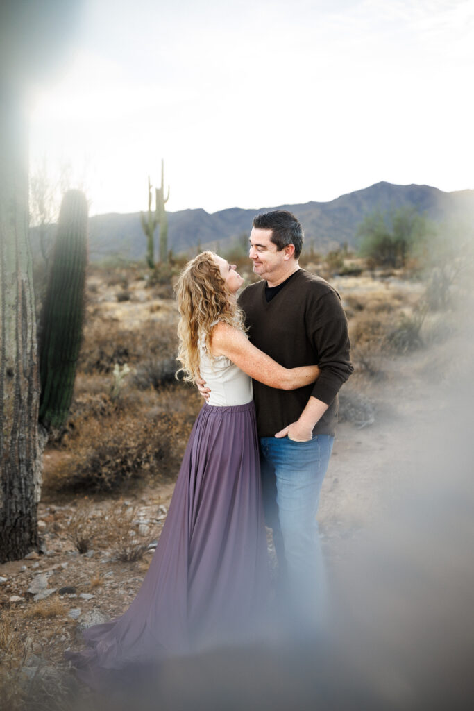 husband and wife hugging while looking into each others eyes. Desert background in phoenix, Arizona