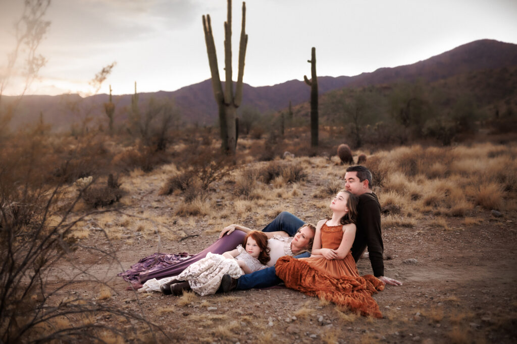 family of four cuddled in the desert as they look off into the sunset