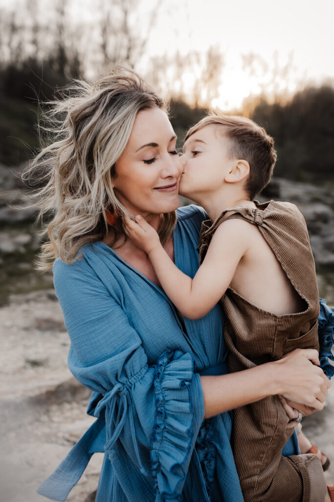 little boy in overalls kissing the cheek of his mother during family photos