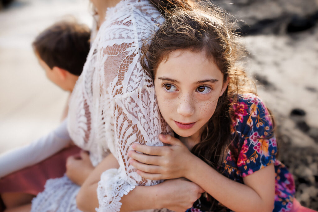 girl holding moms arm on the beach of oahu during family photos