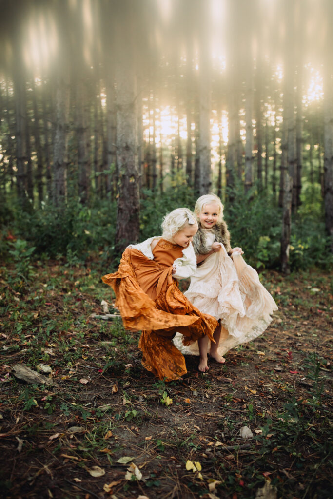 sisters dancing in joyfolie dresses with pine trees in background during family photos