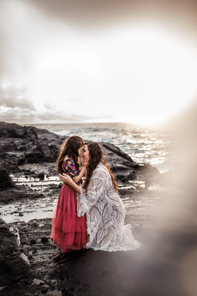 mother and daughter touching foreheads on rocky shoreline of oahu during family photos