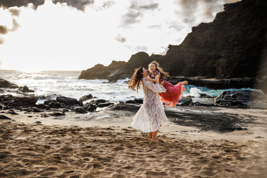 mother twirling daughter in the air along the beach of oahu during family photos