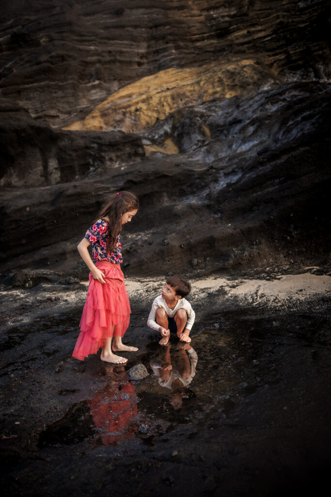 two children playing in puddle near rocky cliff of oahu