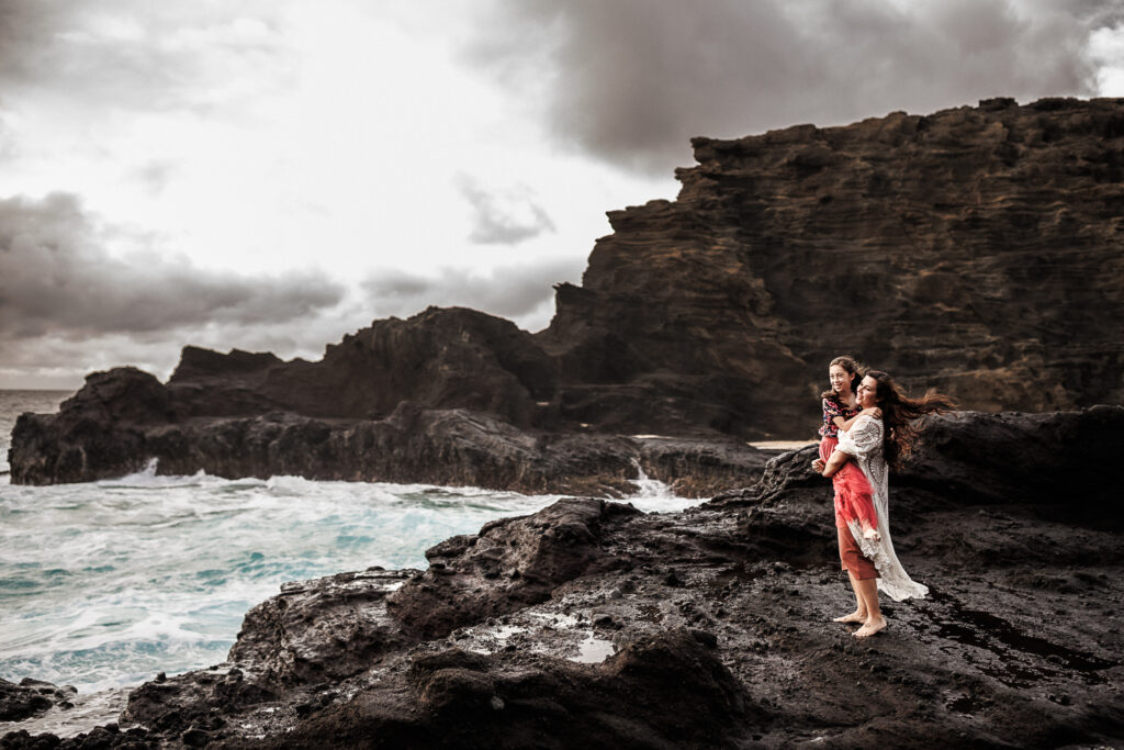 mother holding daughter on rocky cliffs from behind the scenes of a photoshoot