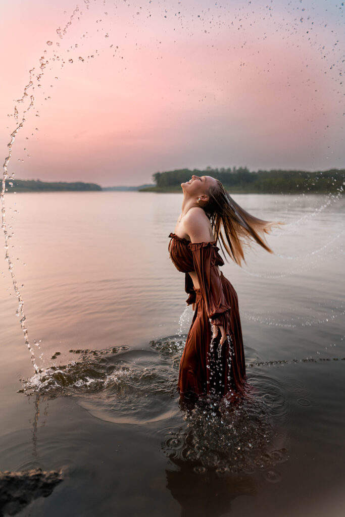 senior pictures in the water with girl doing a hair flip and water spraying in a circle above her