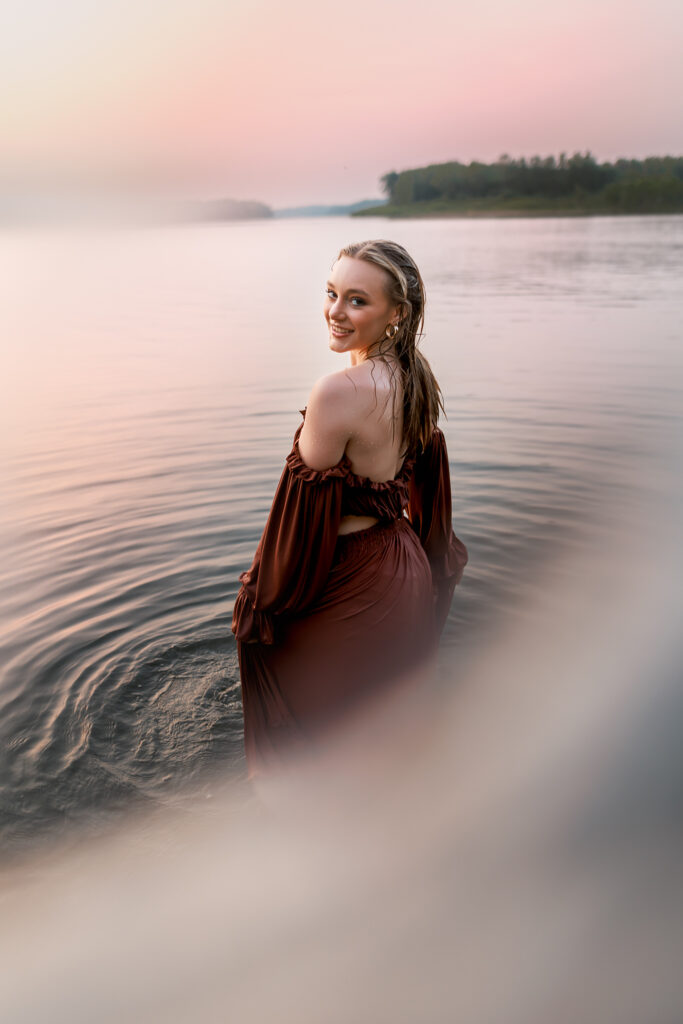 senior photos in the water with hazy photo and girl soaking wet from lake water, smiling into the camera