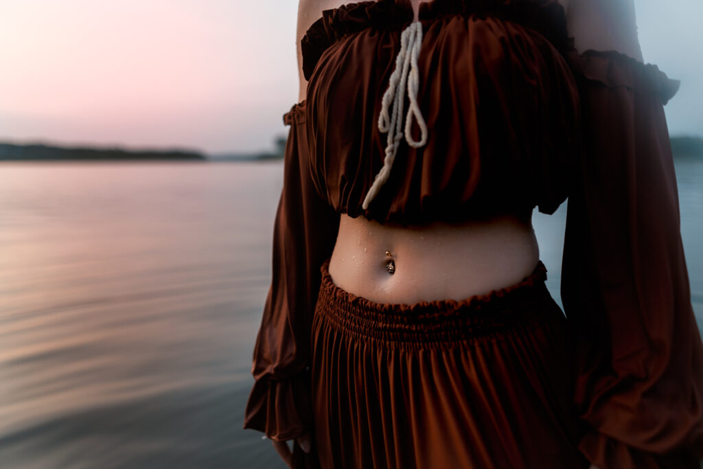 senior pictures in the water with close up photo of girls belly button ring and sun setting behind her