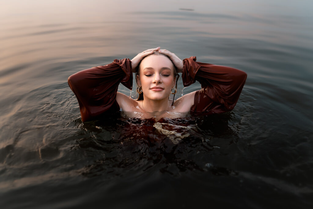 girl brushing water from her hair while eyes are closed nearly fully submerged in lake