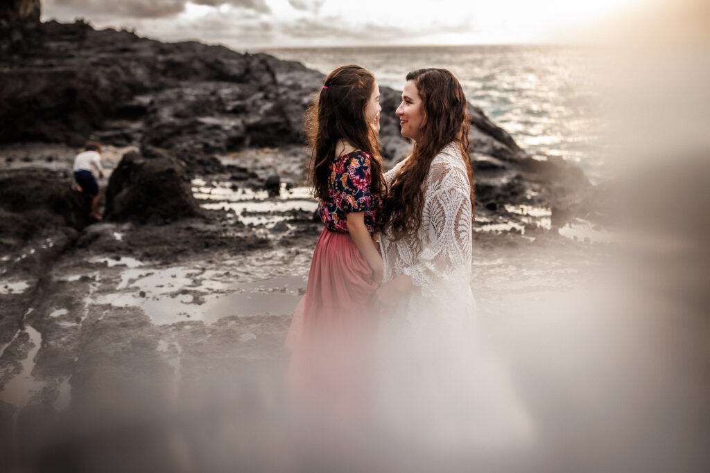 profile portrait of mom and daughter looking at each other with rocks and ocean in background