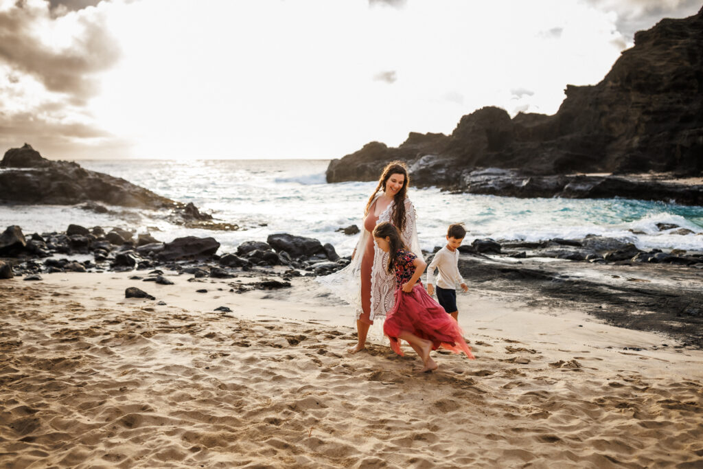 children running around mom on the beach as they chase each other. Everyone is smiling