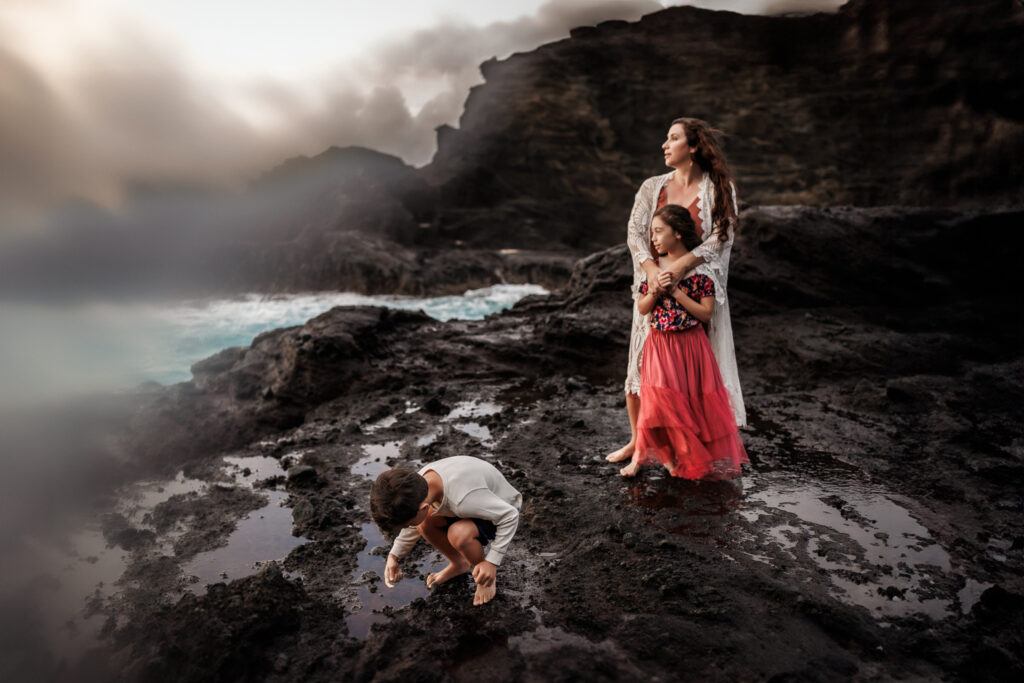 behind the scenes of a photoshoot with mom and children as they stand on the rocky coast of oahu, hawaii