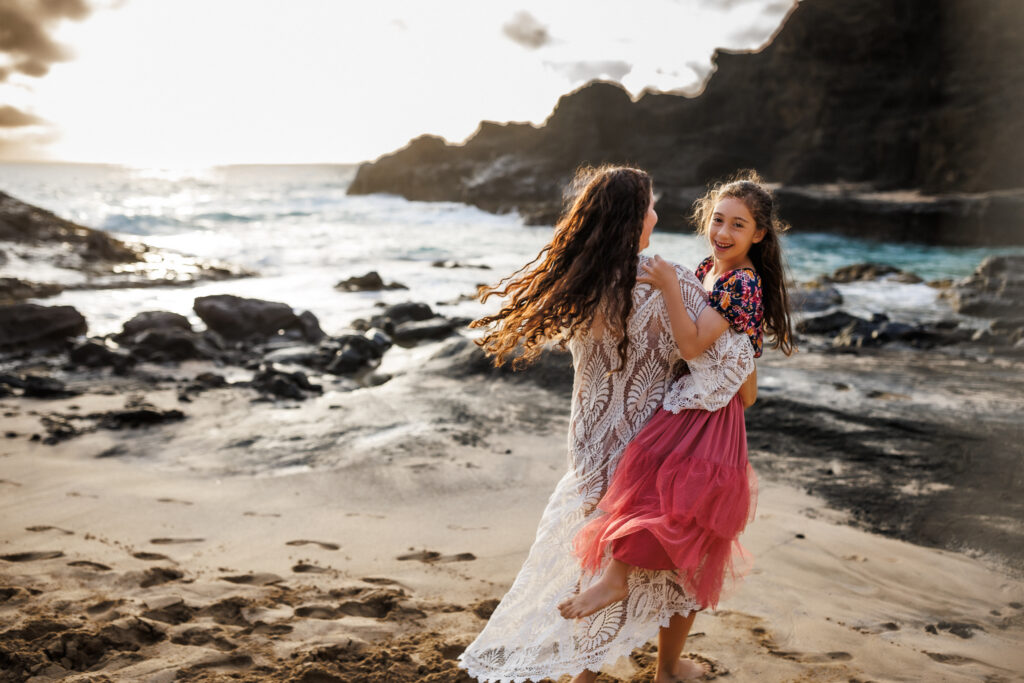 mom carrying little girl on her hip as girl is smiling and running across the sand