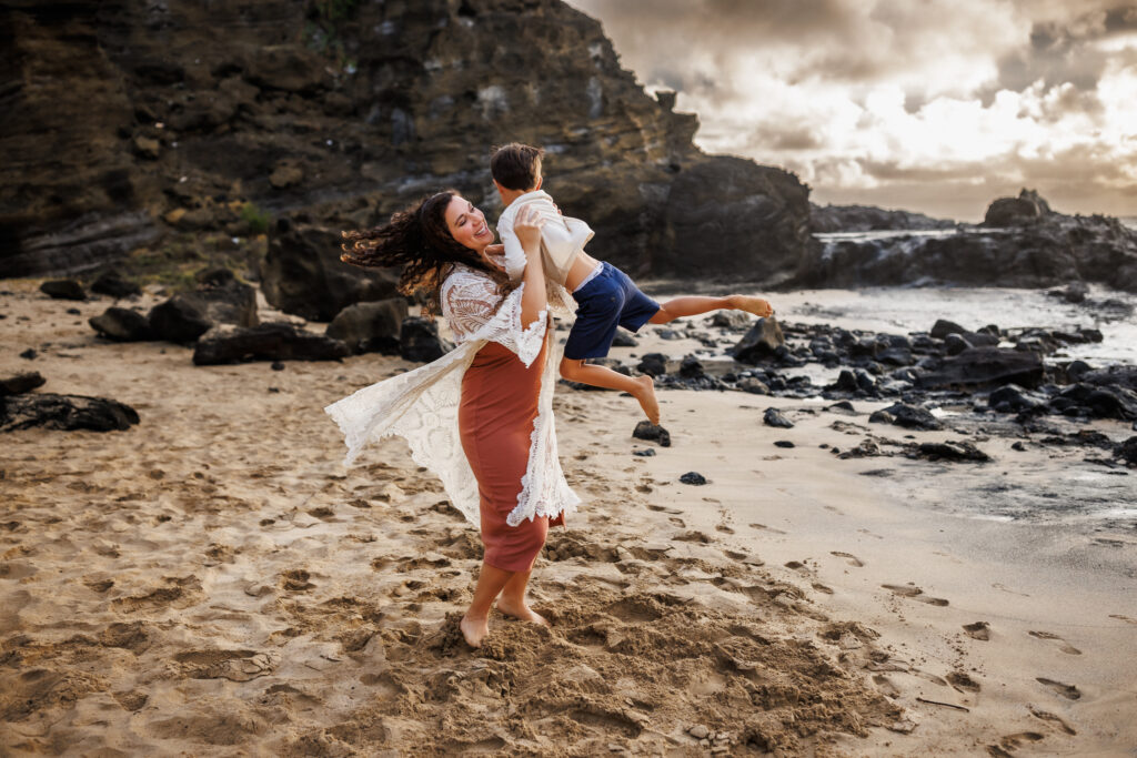 mother swings little boy in the air on the beach during photoshoot