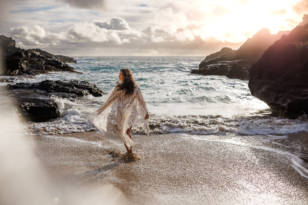 candid photo of woman on the beach with sunrise behind her as her dress flows in the wind